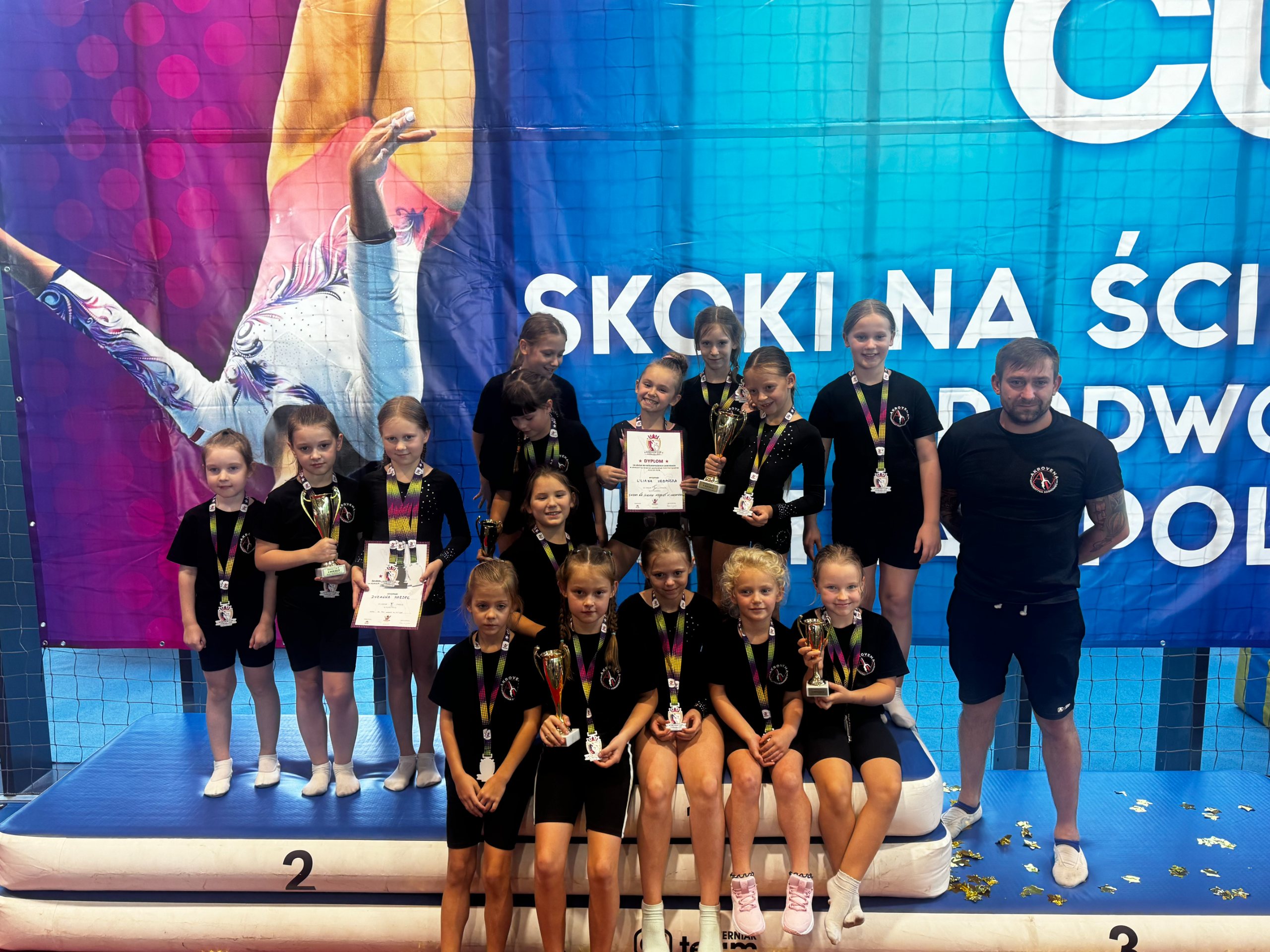 Zawodniczki klubu akrobatyki Akrovena z Sosnowca z trenerem, medalami i pucharami po zawodach
