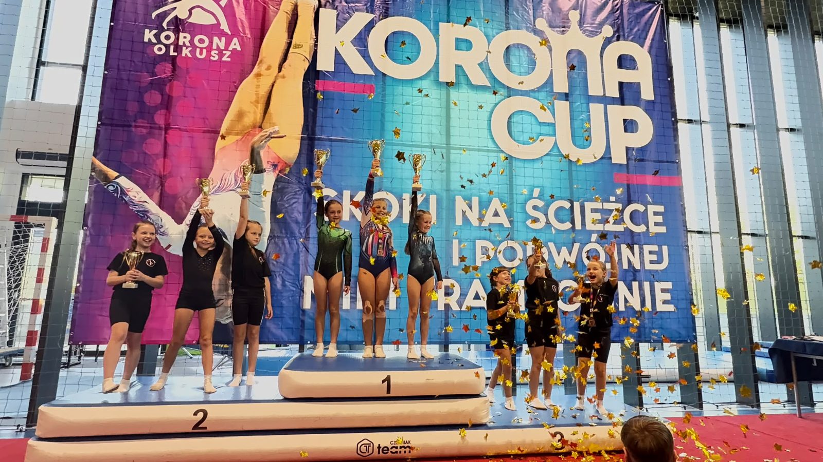 Dekoracja Korona Cup - zawodniczki Akroveny z pucharami w deszczu konfetti